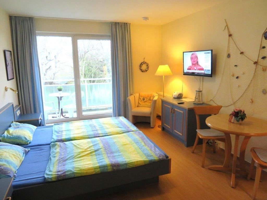 Une chambre d’hôtel avec un lit, un bureau, une chaise, une télévision et un balcon avec des rideaux.