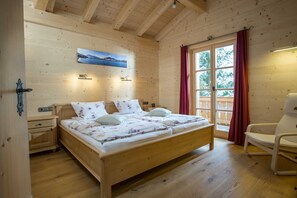 Ett rum med träpanel på väggarna, ett med en säng, en stol, ett nattduksbord, en vägglampa och ett fönster med gardiner.