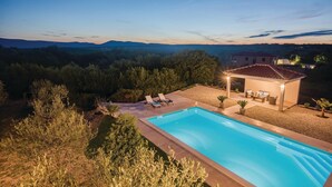 A swimming pool with lounge chairs, a covered seating area, and a view of a forested landscape at dusk. - Awesome apartment in Krk with swimming pool (Krk)