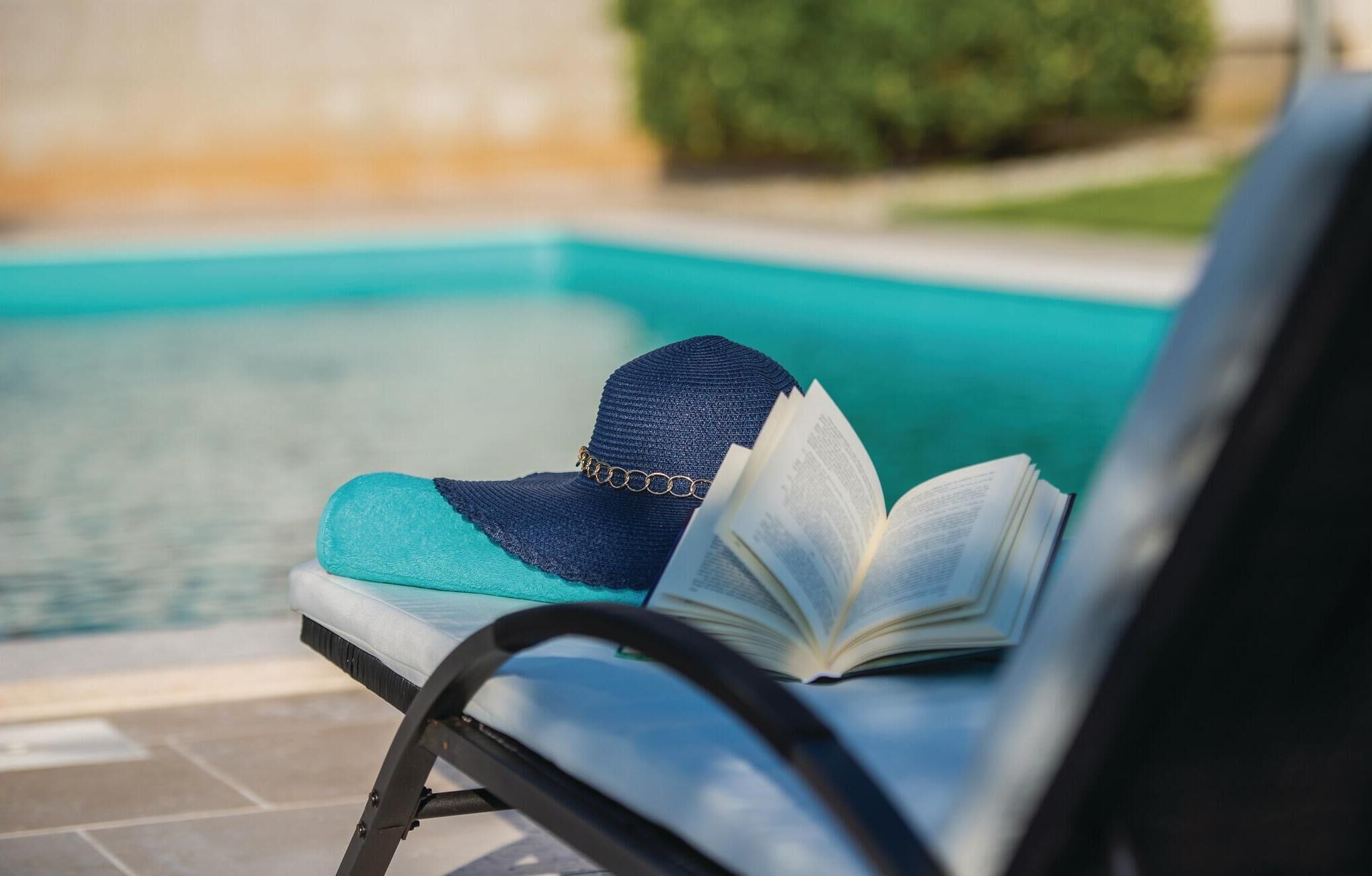 A poolside chair with a book and a hat.