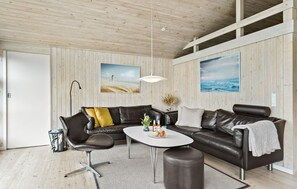 A modern living room with a leather sectional sofa, a white coffee table, and a large window overlooking a beach. - Amazing home in Løkken with sauna (Løkken)