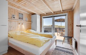 Een slaapkamer met twee bedden, houten wanden, een groot raam en een balkon met tafel en stoel.