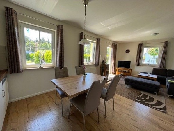 Un vaste espace de vie comprenant une table à manger en bois, deux chaises, un canapé et un téléviseur.