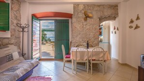 A cozy room with a bed, a dining table with chairs, a small kitchen area, and a view of the sea through an open door. - Beach front home in Podgora with WiFi (Podgora)