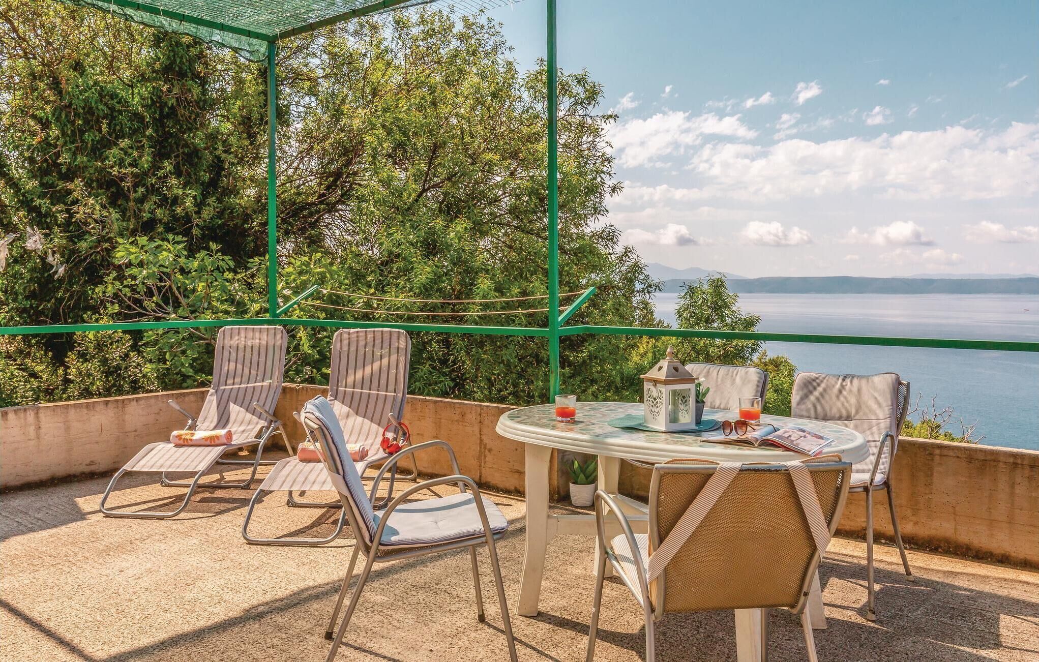 A terrace with a table and chairs, a small table with a plant, and a view of the sea.