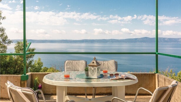 A round table with chairs, a lantern, and a glass of orange juice on a balcony overlooking a large body of water and distant mountains. - Beach front home in Podgora with WiFi (Podgora)