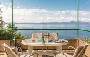A round table with chairs, a lantern, and a glass of orange juice on a balcony overlooking a large body of water and distant mountains. - Beach front home in Podgora with WiFi (Podgora)