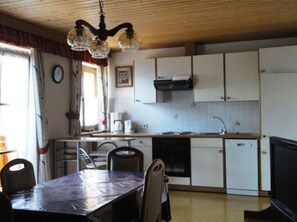 Une cuisine avec des meubles blancs, un lave-vaisselle et un coin repas comprenant une table et des chaises.