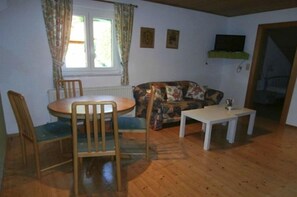Une pièce comprenant une table ronde, deux chaises, un canapé, une petite table blanche et un téléviseur posé sur une étagère.