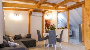 A modern living space with a wooden ceiling, a sofa, a dining table with chairs, and a kitchen area visible through an open archway.