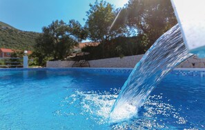 Relax by the pool surrounded by lush trees and a tranquil water feature.