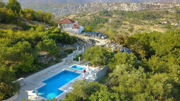 A villa with a swimming pool, surrounded by lush greenery and mountains in the background.