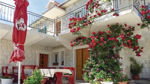 A building with a balcony adorned with red roses, outdoor seating, and a red umbrella.