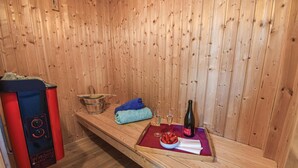 Et sauna-rum med trævægge, en bænk, en spand, håndklæder, glas og en flaske.