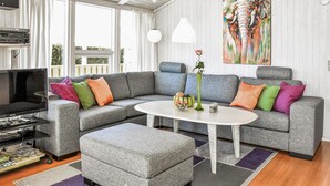 En moderne stue med en grå hjørnesofa, et hvidt sofabord og et fjernsyn på et stativ.
