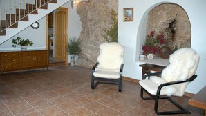 A spacious living area with a stone wall, two white armchairs, a wooden staircase, and a dining table with a vase of flowers.