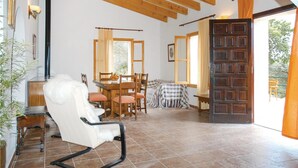 A spacious room with a wooden ceiling, a dining area with a table and chairs, a large wooden door, and a view of the outdoors.