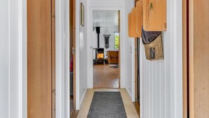 Käytävällä on puiset ovet, takka ja punottu kori, jossa on kyltti, jossa lukee: ”Vieraille”.