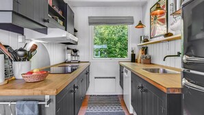 Moderni keittiö, jossa on tummat kaapit, puutasot, sisäänrakennettu liesi ja ikkuna, josta avautuu näkymä vehreään maisemaan.