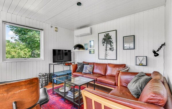 Ett modernt vardagsrum med en soffa i läder, ett soffbord i glas och en tv som står på ett stativ.