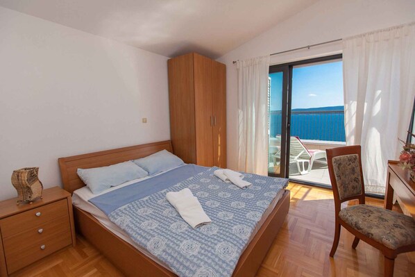 A bedroom with a bed, wooden wardrobe, chair, and a balcony with a view.