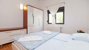 Een slaapkamer met een bed, nachtkastje, kast, raam met gordijnen en een radiator.