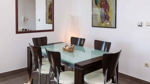 Een eetgedeelte met een tafel met glazen blad, vier stoelen en twee kunstwerken in lijsten aan de wanden.