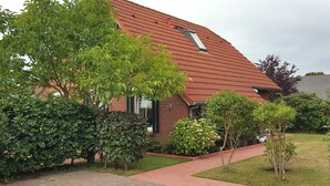 A house with a red tiled roof, a brick facade, and a paved driveway leading to the entrance. - Vacation home in Nessmersiel 20-014a - 200-014a (Dornum)