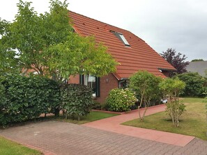 Uma casa com telhado de telhas vermelhas, fachada de tijolos e um caminho de paralelepípedos que leva à entrada.