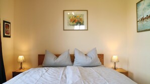 A neatly made bed with striped bedding, two bedside lamps, and a framed floral painting on the wall.