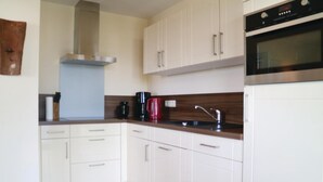 A modern kitchen with white cabinets, a stainless steel range hood, a black oven, and a wooden countertop.