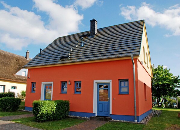 A single-story house with a sloped roof, a blue door, and a small front garden.