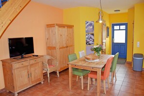 Ein Essbereich mit Holztisch, Stühlen, einem Fernseher auf einer Holzkommode und einer Treppe, die zu einer oberen Ebene führt.