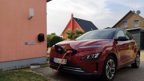 Ein rotes Auto vor einem Gebäude, an dem ein Schild mit der Aufschrift "Nur für Elektrofahrzeuge Ladenschluss" steht.