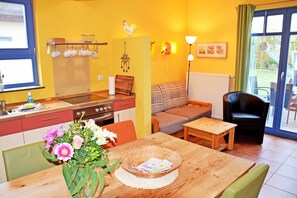 Ein helles, gelbes Zimmer mit einer Küche, einer Essecke mit Tisch und Stühlen sowie einem Sofa.