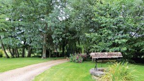A gravel path leading through a lush garden with dense trees and a rustic wooden structure. - Gorgeous home in Vernie with WiFi (Vernie)
