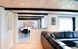 En moderne stue med en lædersofa, et spiseområde med bord og stole, og et køkken, der kan ses gennem en bue.