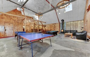 Et rummeligt indendørs område med et pingpongbord, et billardbord og et hyggeligt opholdsområde med pejs.