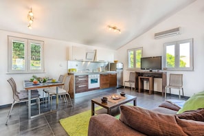 A modern kitchen with a dining area, a TV, and a sofa.