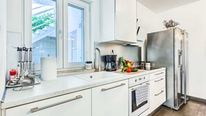 Une cuisine moderne avec des meubles blancs, un réfrigérateur en acier inoxydable et une fenêtre donnant sur un paysage verdoyant.
