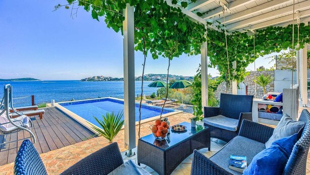 Un espace aménagé au bord de la piscine, avec des meubles en osier, une table sur laquelle est posé un saladier rempli de fruits, et une vue sur la mer.