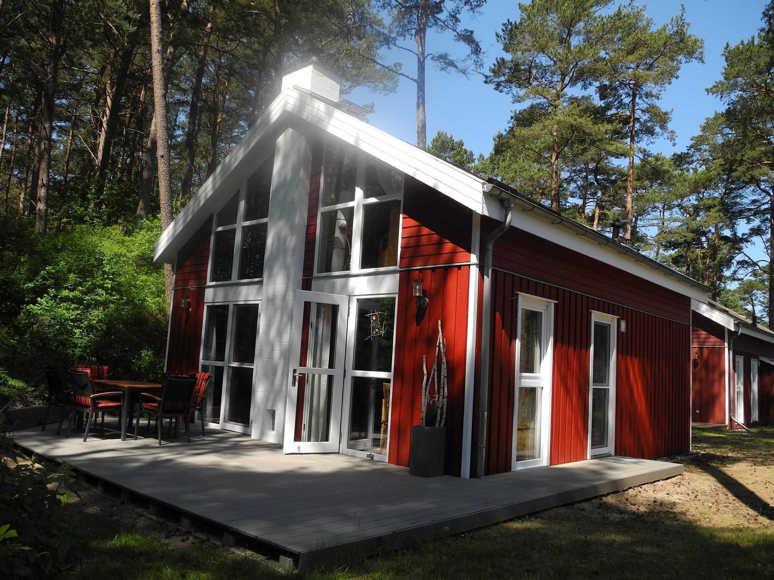 A red cabin with large windows, a deck, and a forest backdrop.
