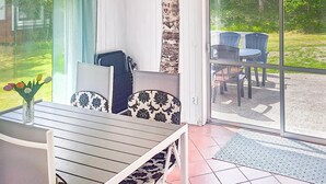 A sunlit patio with a wooden table and chairs, a vase with flowers, and a view of a garden through a glass door. - Stunning home in Annerstad with WiFi (Annerstad)