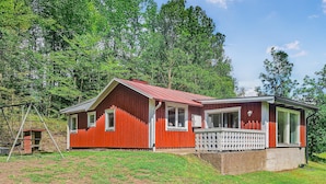 A red wooden house with a white fence, a porch, and a small shed in a grassy area with trees in the background. - Stunning home in Annerstad with WiFi (Annerstad)