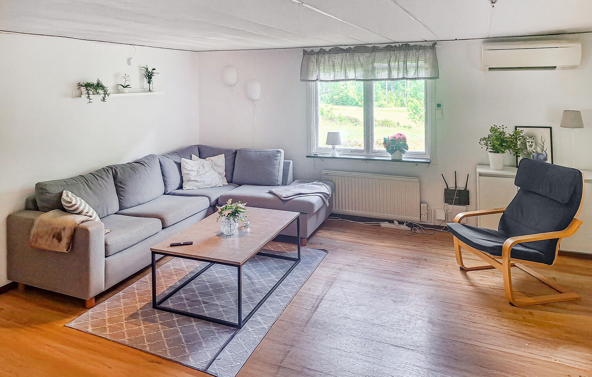A living room with a grey sofa, a wooden coffee table, a black armchair, and a window with a view of greenery.