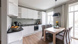 Eine moderne Küche mit weißen Schränken, einem Holzespeisetisch, Korbstühlen und einem großen Fenster mit Vorhängen.