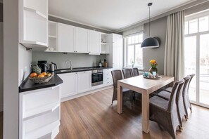 Eine moderne Küche mit weißen Schränken, einem Holzespeisetisch, Korbstühlen und einem großen Fenster mit Vorhängen.