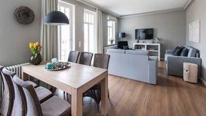 Ein modernes Wohnzimmer mit Essbereich, grauen Sofas, einem Fernseher und einem großen Fenster.
