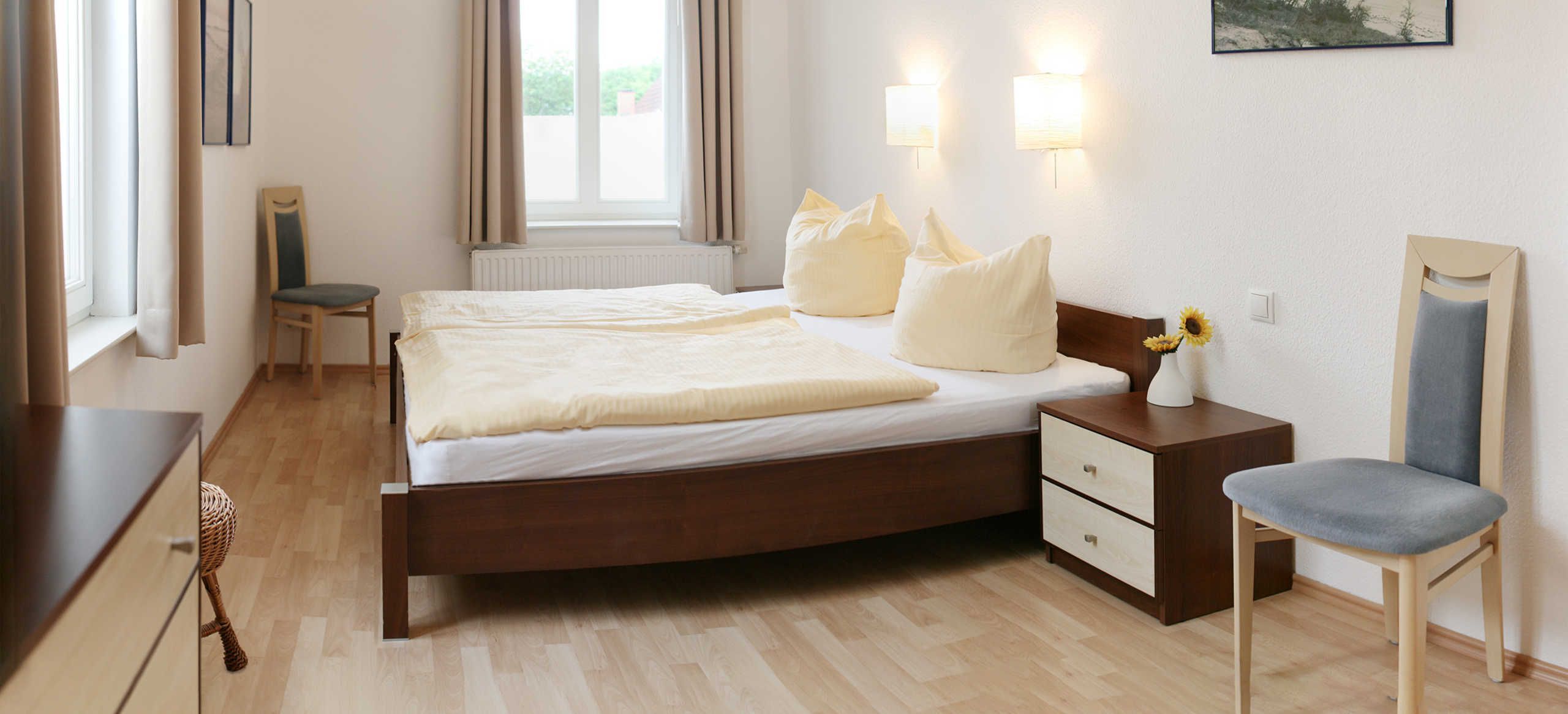 A bedroom with a wooden bed, two bedside tables, a chair, a nightstand, and a window with curtains.