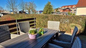 An outdoor seating area with wicker furniture, a wooden table, and potted plants. - Vacation home Boddenblick (Barth)